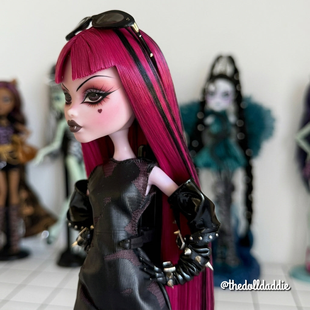 Side profile close-up custom reroot example of Cerise Pink saran doll hair on Monster High Draculaura by @thedolldaddie. Highlight shot showing the sleek hair texture, blunt bangs with black streak accents, and black sunglasses resting on top of the head.