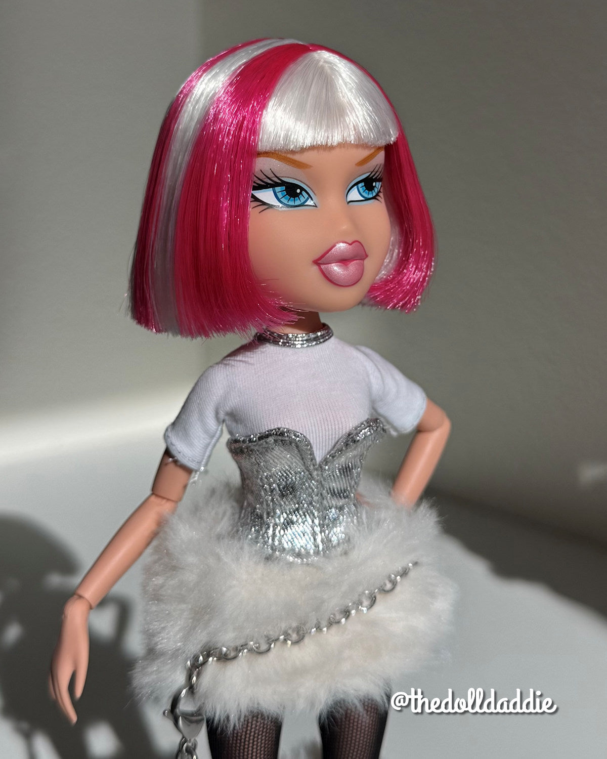 Three-quarter angle of custom Bratz Charmz Cloe rerooted with Shimmer Locks Dragonfruit hot pink and Ivory white saran doll hair by @thedolldaddie. Highlights the blunt bob cut, front bangs, and two-tone color contrast under direct light.