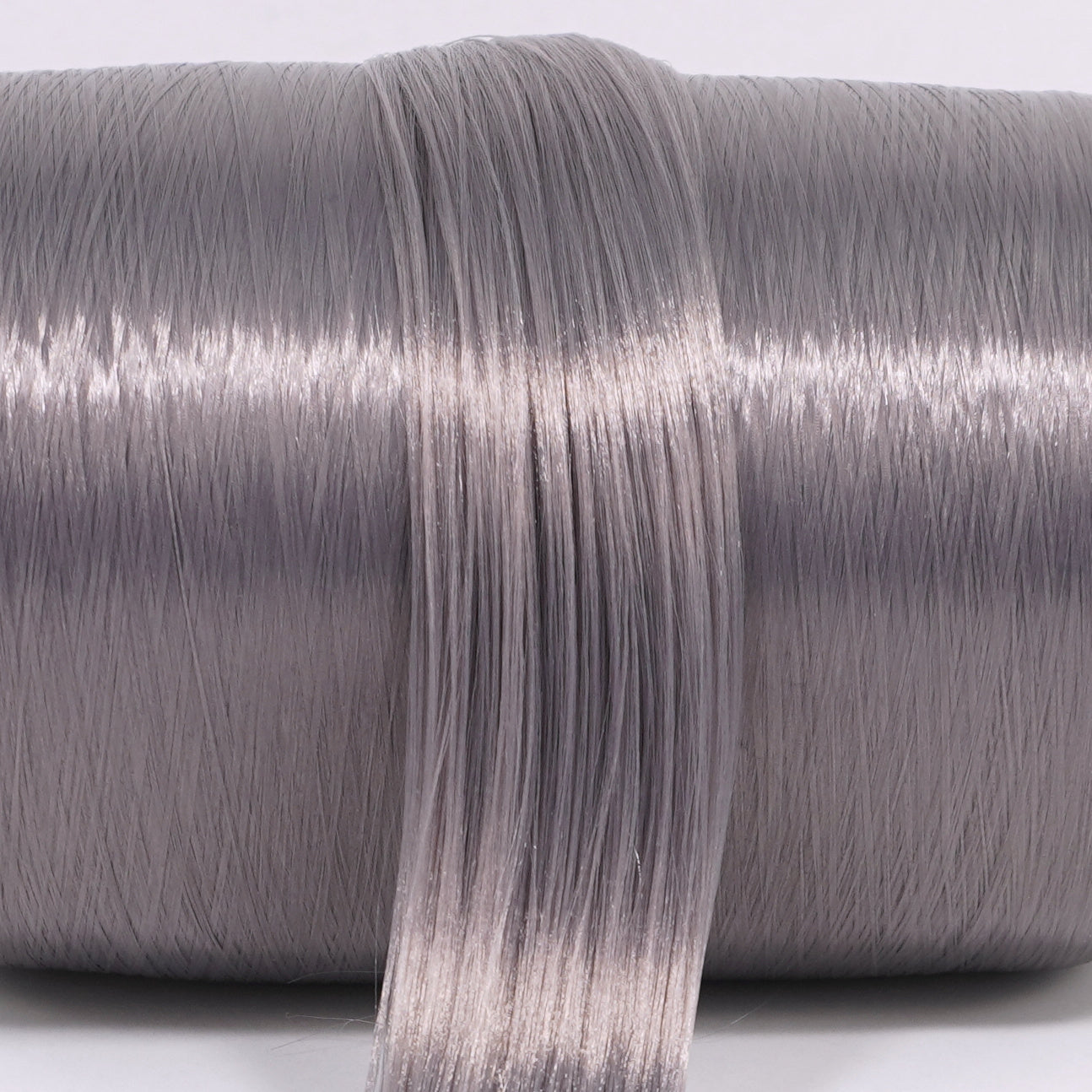 A hank of eclipse gray nylon doll hair laying across a roll. The dark gray has a subtle purple/violet hue for one of a kind custom reroots.