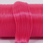 Pizzazz hot pink nylon doll hair hank for rerooting laying across a roll of the same color.