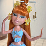 Close-up custom reroot example of Safari Auburn saran doll hair on Bratz Pop Starz Jade by @thedolldaddie. Medium shot highlighting the straight hair length, blunt bangs, high topknot bun with hair chopsticks, and yellow flower accessories.
