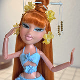 Close-up custom reroot example of Safari Auburn saran doll hair on Bratz Pop Starz Jade by @thedolldaddie. Medium shot highlighting the straight hair length, blunt bangs, high topknot bun with hair chopsticks, and yellow flower accessories.