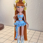 Full-length custom reroot example of Safari Auburn saran doll hair on Bratz Pop Starz Jade by @thedolldaddie. Full shot displaying the waist-length straight hair, styled topknot bun, blunt bangs, and light blue outfit.